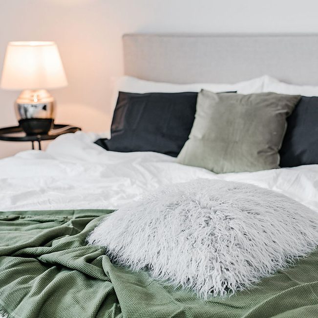 sovrum med fokus på säng i ljus mossgrönt och vitt lampa och bord i bakgrund